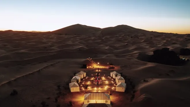 A desert camp illuminated by lights, set against the vast, serene backdrop of the desert landscape Morocco desert night