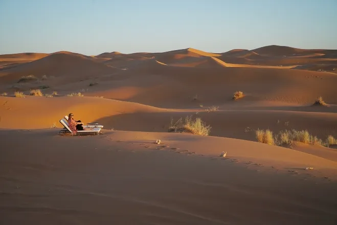 A person seated in a chair, surrounded by vast desert landscape under a clear blue sky Morocco desert night