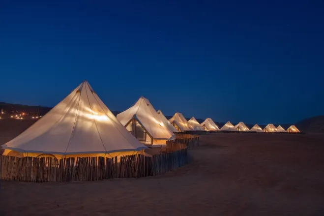 Tents illuminated at night in a serene desert landscape, showcasing a tranquil atmosphere under the starry sky morocco desert tour