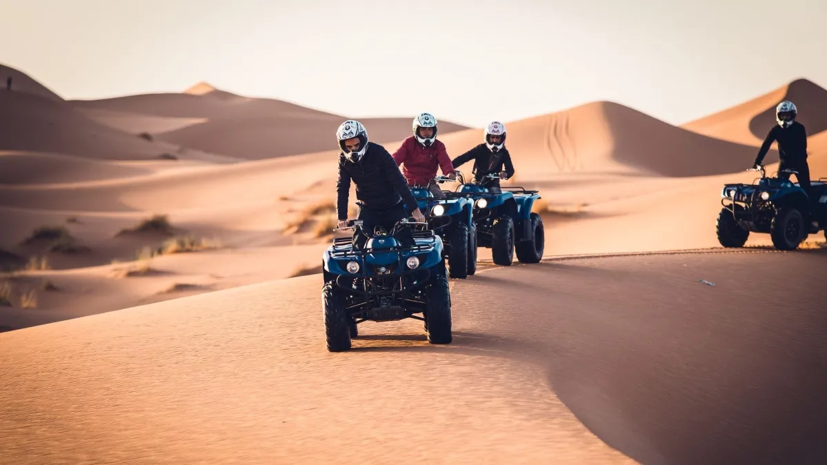 Four individuals riding quad bikes across a vast desert landscape under a clear blue sky Erg Chebbi Dunes