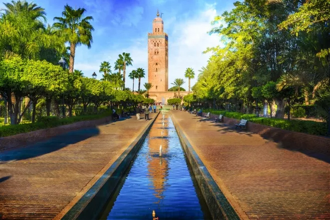 The clock tower of the Hajj Mosque in Marrakech, Morocco, stands tall against a clear blue sky, showcasing intricate architecture morocco tour