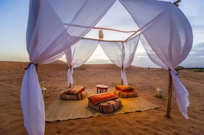 A tent adorned with white drapes set against the backdrop of the morocco desert camp landscape.