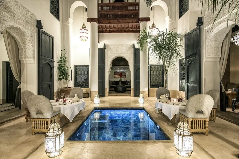 Elegant dining area in a riad with white walls and a tranquil pool, perfect for guests on a luxury Sahara desert tour from Marrakech. 