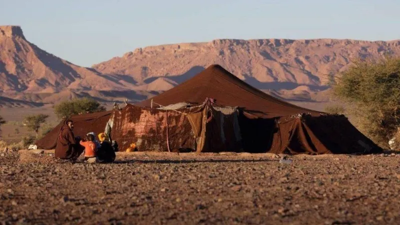 A tent in the Sahara desert sunrise, with majestic mountains rising in the background, creating a serene landscape