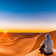 A Woman sits on the sand dunes of the Sahara Desert at sunset, capturing the serene beauty of Morocco's landscape.