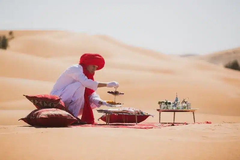 A Man in a red headscarf prepares food in the Sahara desert during a Fes to Sahara tour.