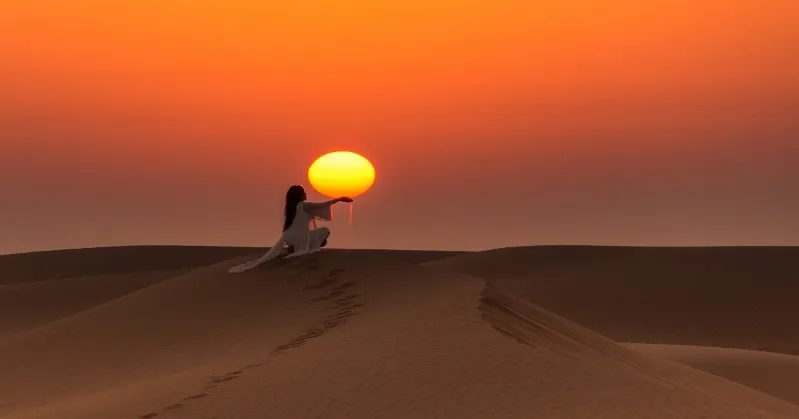 A woman stands in the Sahara Desert, holding an orange ball, showcasing the vibrant contrast of color against the sandy landscape.