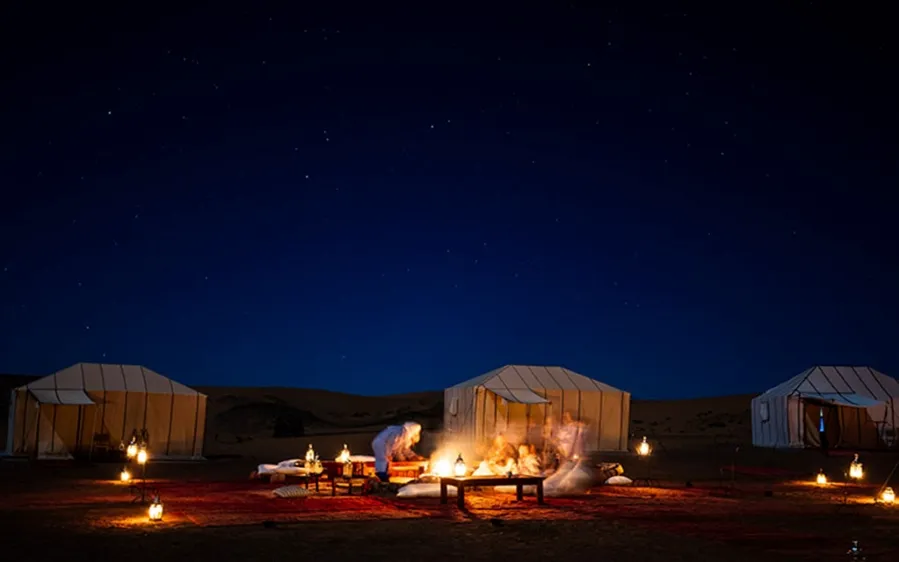 A group of people gathered around a campfire in the Moroccan desert, illuminated by the night sky.