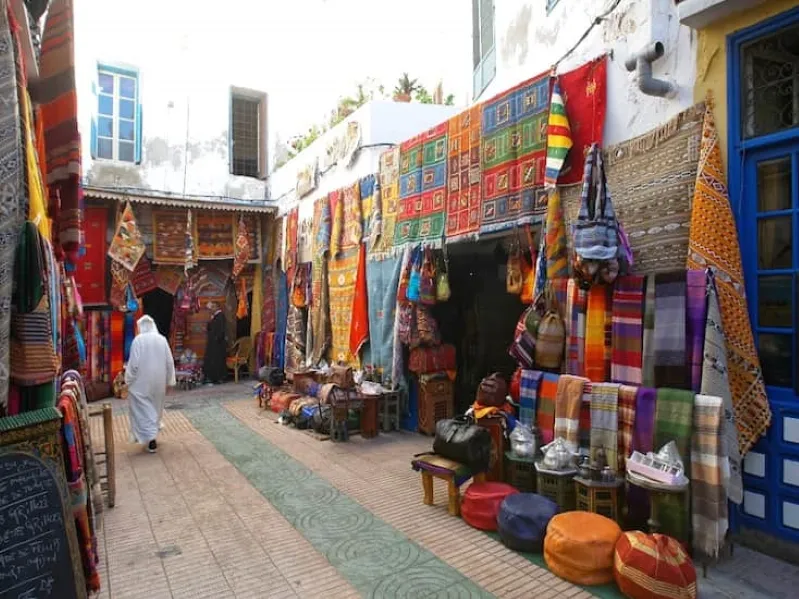 A narrow Souks in Morocco alley adorned with vibrant carpets, featuring a man walking through the colorful display.