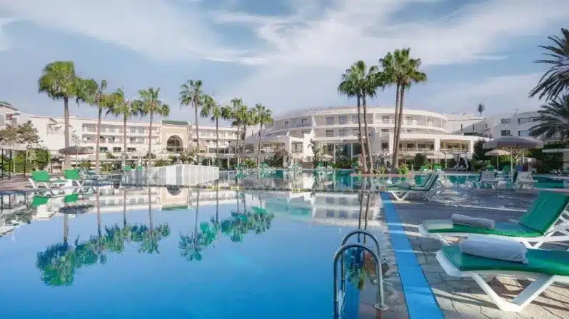 A serene hotel pool surrounded by lounge chairs and palm trees, perfect for Agadir beach holidays.