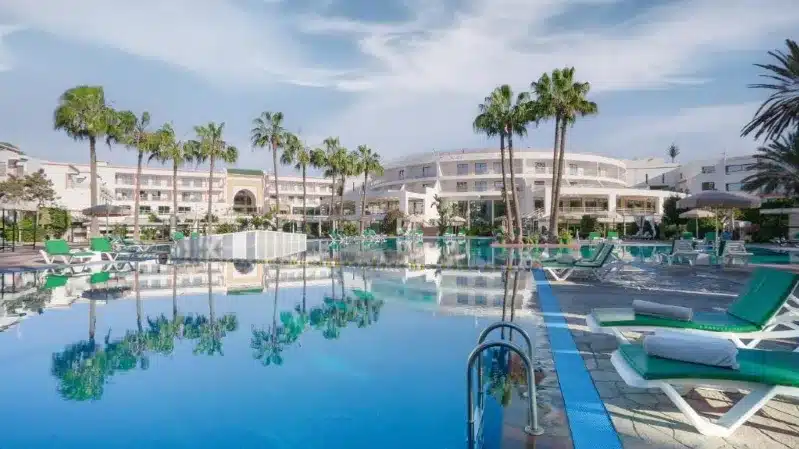 A serene hotel pool surrounded by lounge chairs and palm trees, perfect for Agadir beach holidays.