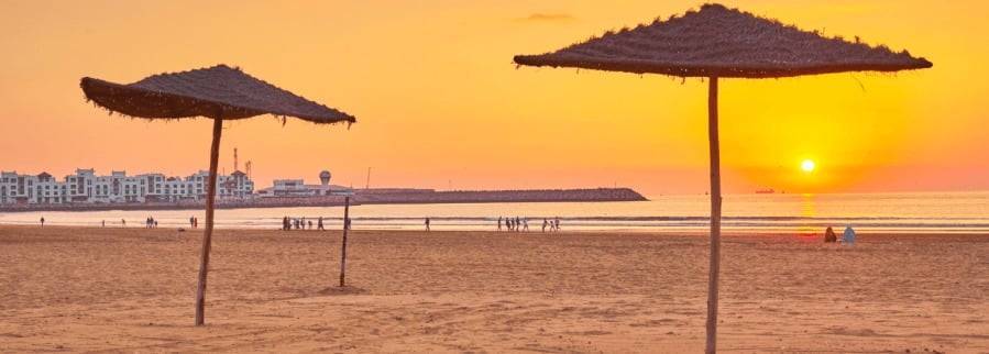 A serene sunset over Agadir beach in Morocco, casting warm hues across the tranquil waters and sandy shore.