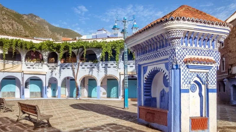 A scenic courtyard featuring blue and white buildings, nestled amidst majestic mountains in Tangier. 