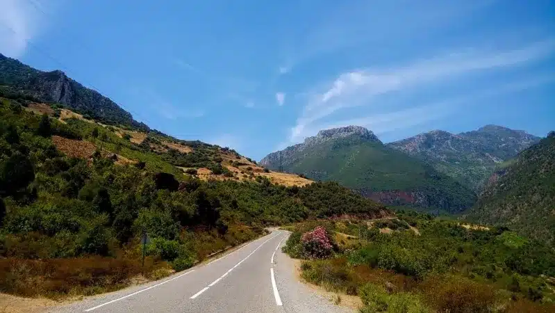 A picturesque road winding through mountains, framed by a vibrant blue sky, ideal for a Morocco road trip.
