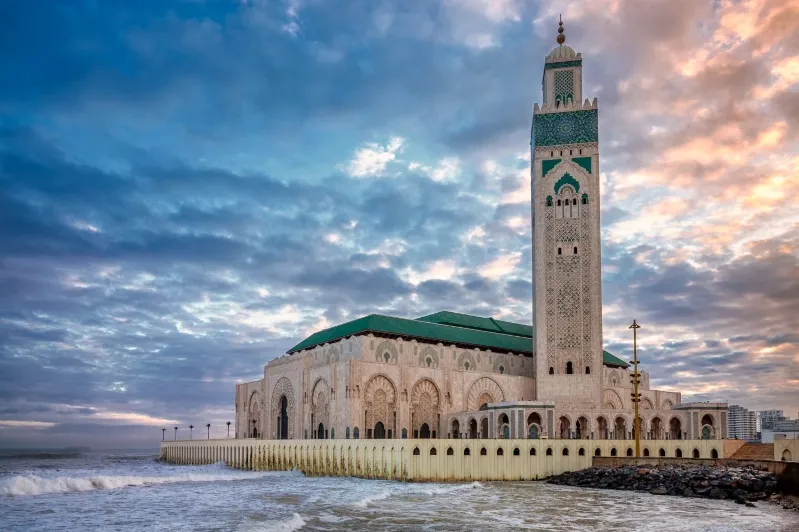 A stunning mosque on the beach in Casablanca, illuminated by the warm hues of a sunset, showcasing a popular casablanca tourist attractions.