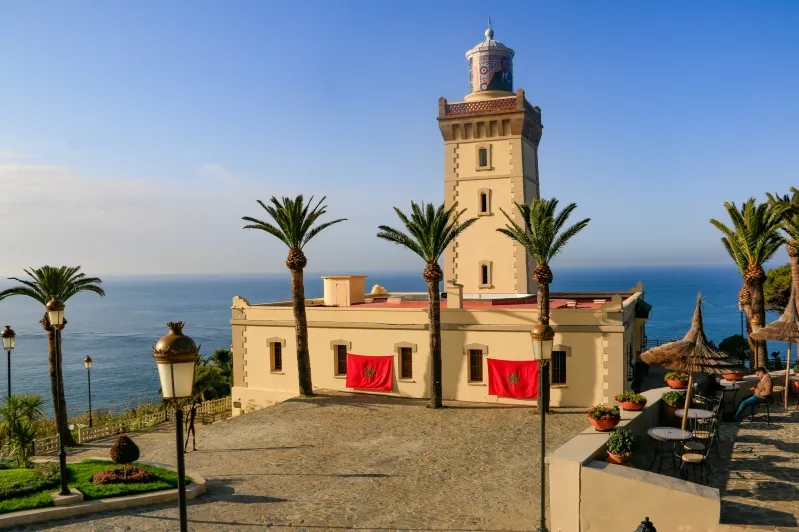 A picturesque lighthouse stands on the coast, surrounded by palm trees, showcasing Tangier's scenic beauty.