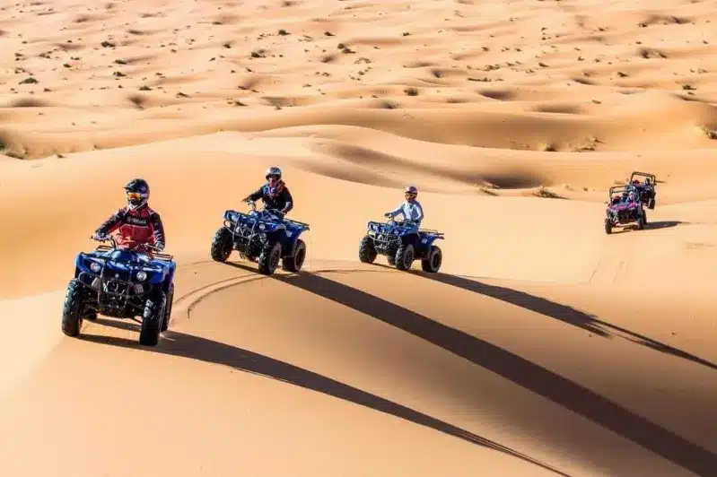 A group of four adventurers navigating quad bikes through the stunning desert terrain of morocco best sahara tours. 