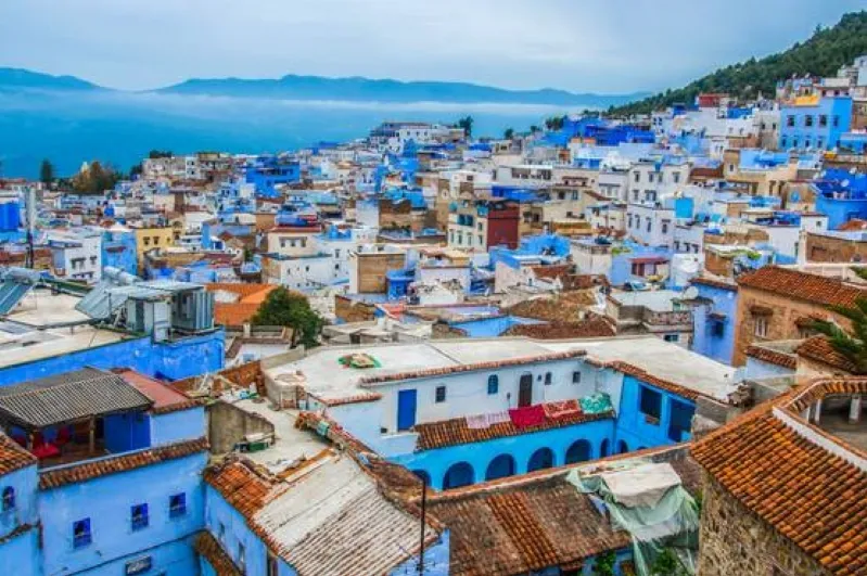 Aerial view of Chefchaouen, Morocco, with blue-painted buildings and distant mountains.