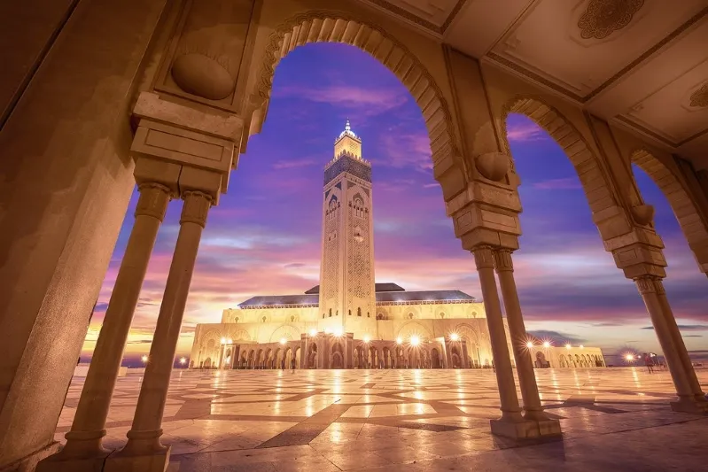 A stunning sunset casts a golden light on the mosque, creating a picturesque scene, perfect for where to Travel Morocco.