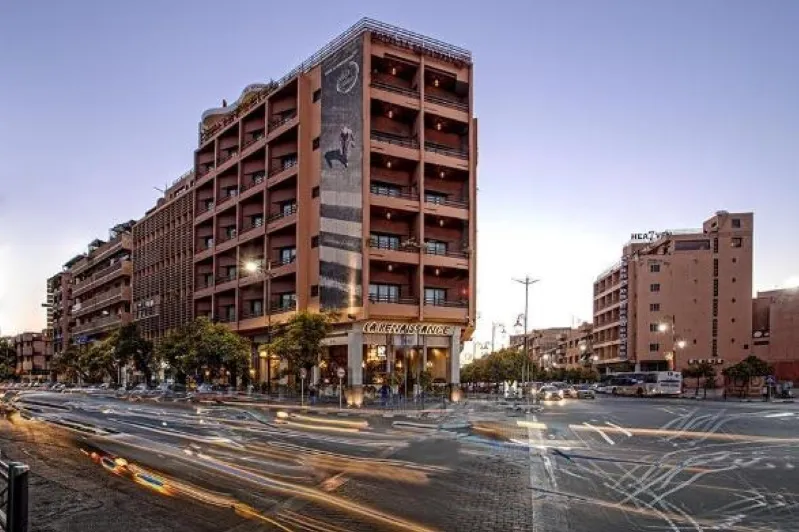 A bustling street view in Gueliz, Marrakesh, featuring a building with cars passing by, showcasing vibrant gueliz marrakesch shopping activity. 