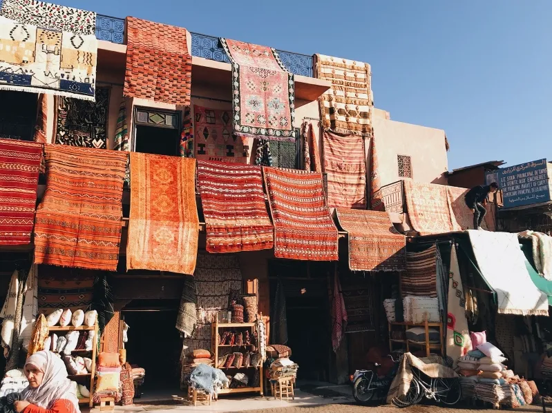 A vibrant market with colorful rugs and textiles displayed on a building's facade.