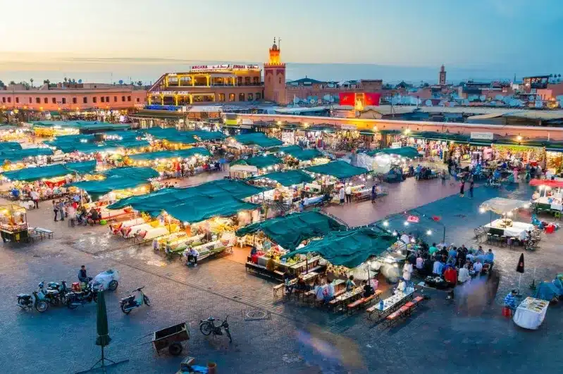 A vibrant Marrakesh market at dusk, showcasing colorful stalls and bustling activity, perfect for Morocco travel deals.
