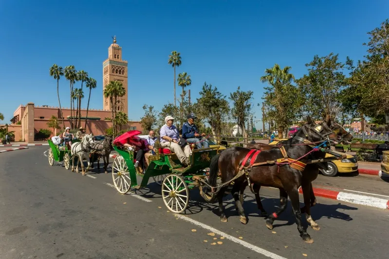 Tourists enjoy a horse-drawn carriage ride near a clock tower, highlighting a popular attraction in Marrakech.