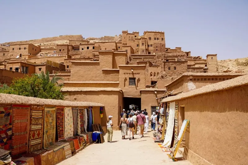People navigate a narrow alleyway in the desert, surrounded by historical sites in Morocco. 