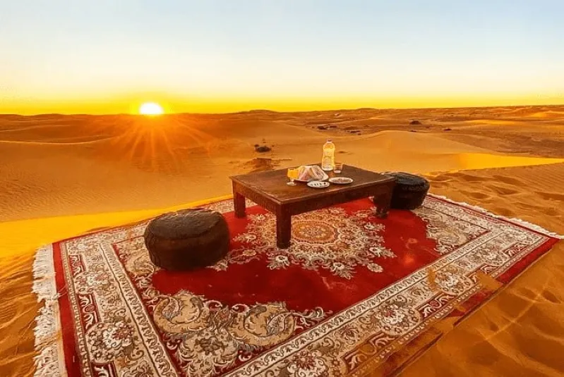 A rug, table, and chairs are arranged in the desert, highlighting Morocco's historical sites and cultural richness. 