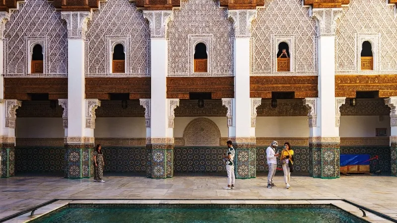 Individuals stand near an indoor pool in a historical sites in Morocco, highlighting the beauty of oriental design. 