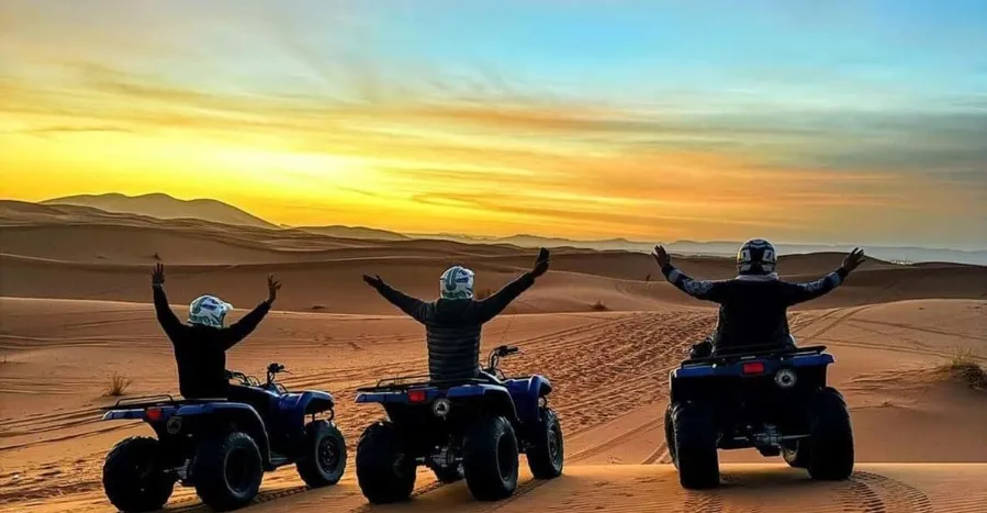 Four individuals riding ATVs through the Moroccan desert during a vibrant sunset, showcasing adventure and natural beauty.