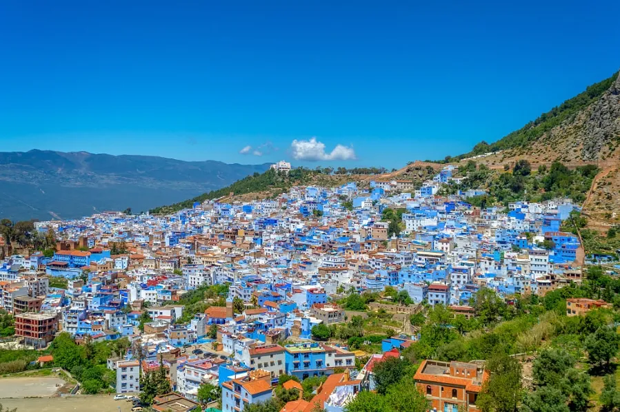 A panoramic view of Chefchaouen, the blue city of Morocco, nestled between green hills.