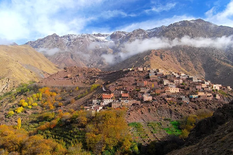 A picturesque village nestled in the mountains, with the majestic Atlas Mountains range towering in the background.