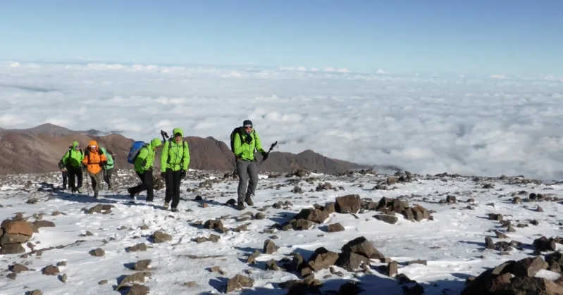 A group of individuals in green jackets ascends a snowy slope in the High Atlas Mountains.