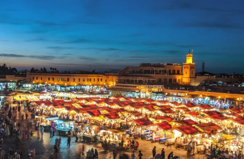 A vibrant Marrakesh market at dusk, showcasing colorful stalls and bustling activity under a twilight sky.