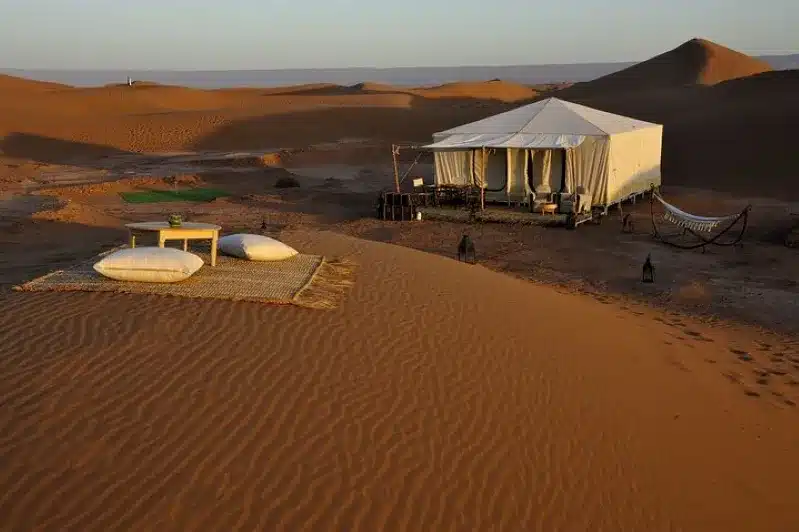 A tent in the desert featuring a table and chairs, set against the backdrop of a 10-day Morocco tour from Casablanca.