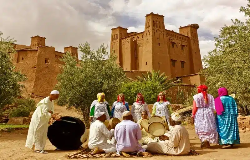 A group of Berber people from Morocco in traditional attire, energetically playing drums together in a vibrant setting.
