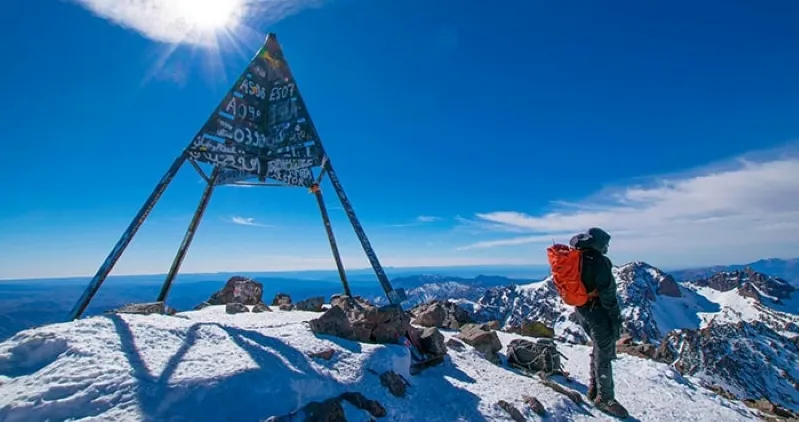 A hiker stands atop a peak in the Atlas Mountains, gazing at the breathtaking landscape with a backpack on their back.