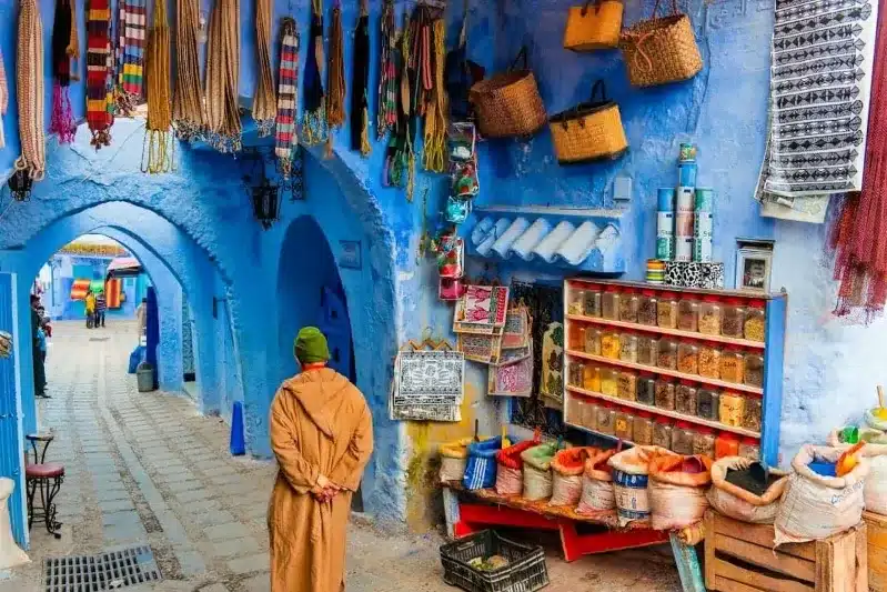  A man in a blue robe strolls through a narrow alleyway while sightseeing agadir.