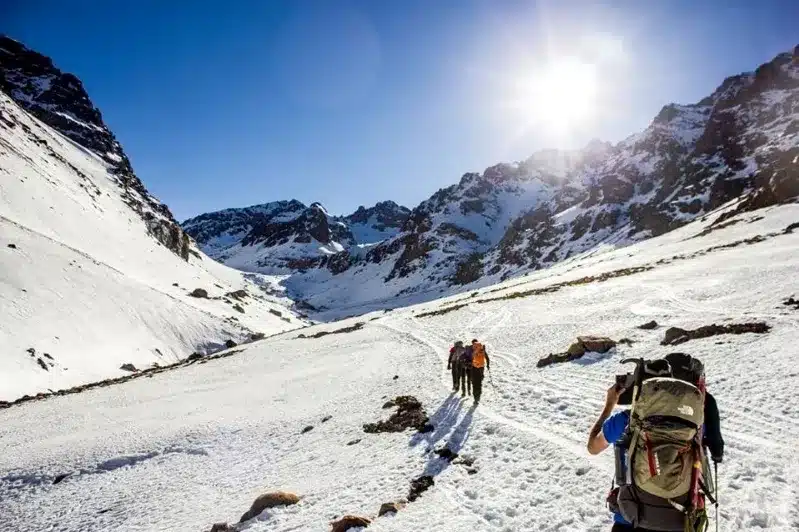 Two hikers with backpacks trek through snow-covered mountains, showcasing the beauty of winter landscapes in Morocco.