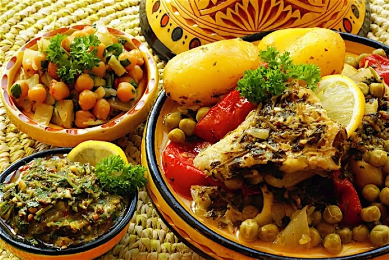 A colorful assortment of Moroccan dishes featuring fish, fresh vegetables, and traditional bread on a vibrant table setting.