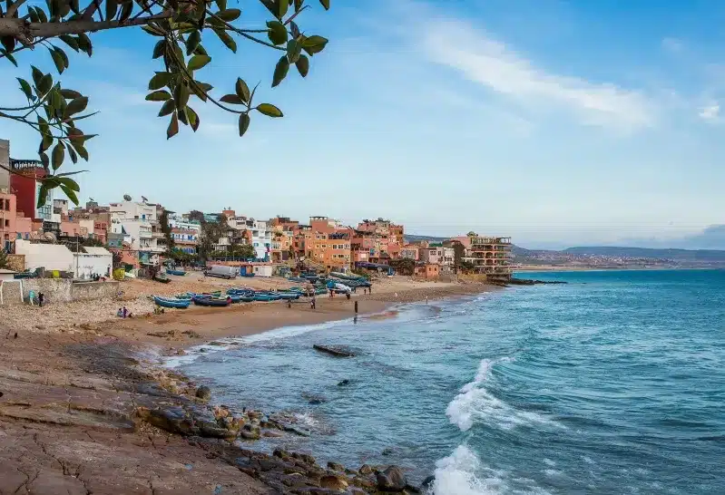A vibrant beach in Morocco featuring colorful houses under a clear blue sky, ideal for travel in spring or fall.