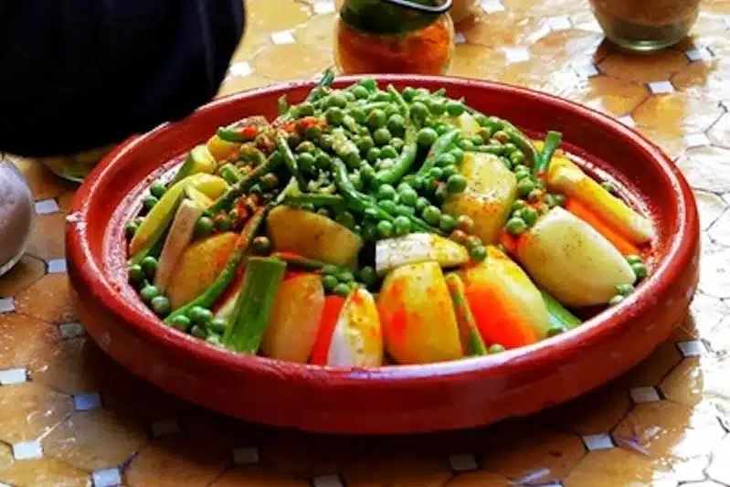 A plate of beef Moroccan tagine garnished with vibrant vegetables and aromatic spices on a rustic table.