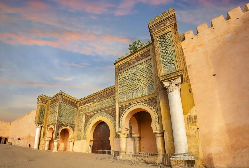 Entrance to Marrakech, Morocco, featuring traditional architecture and a camel ride in the background.
