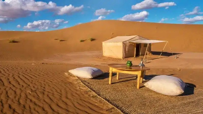 A tent set up in the desert, featuring a table and chairs, ideal for travelers exploring Morocco's landscapes.