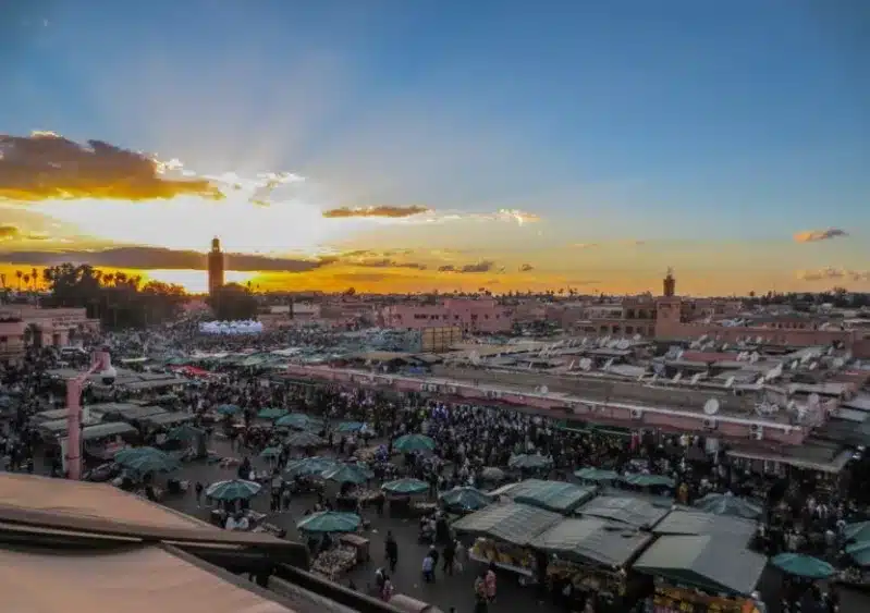 A vibrant sunset casts warm hues over Marrakech, with a hint of Moroccan food in the foreground, showcasing the city's charm.