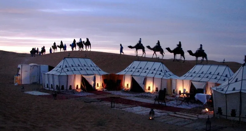 A group of tents in the desert with people riding camels, celebrating casablanca new year.