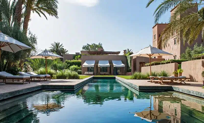 A serene pool area at a Morocco Luxury Hotel, complete with lounge chairs and umbrellas in front of a stylish house. 