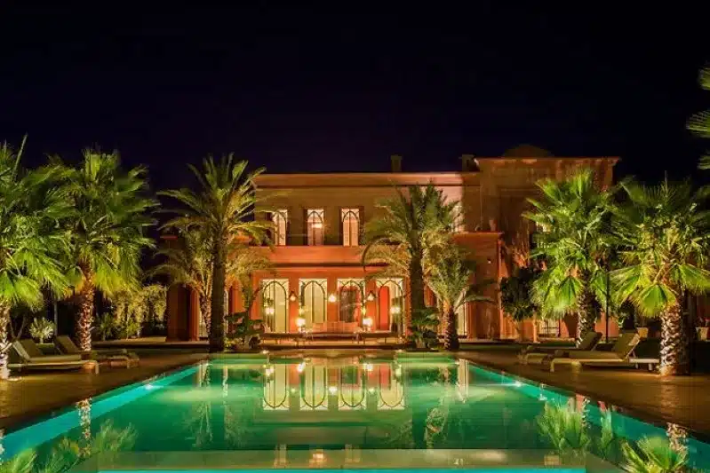 Night view of a luxurious villa in Morocco, with a serene pool illuminated by soft lights reflecting on the water's surface.