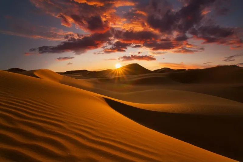 A stunning sunset over the Sahara Desert in Morocco, with silhouettes of camels riding across the sandy dunes.